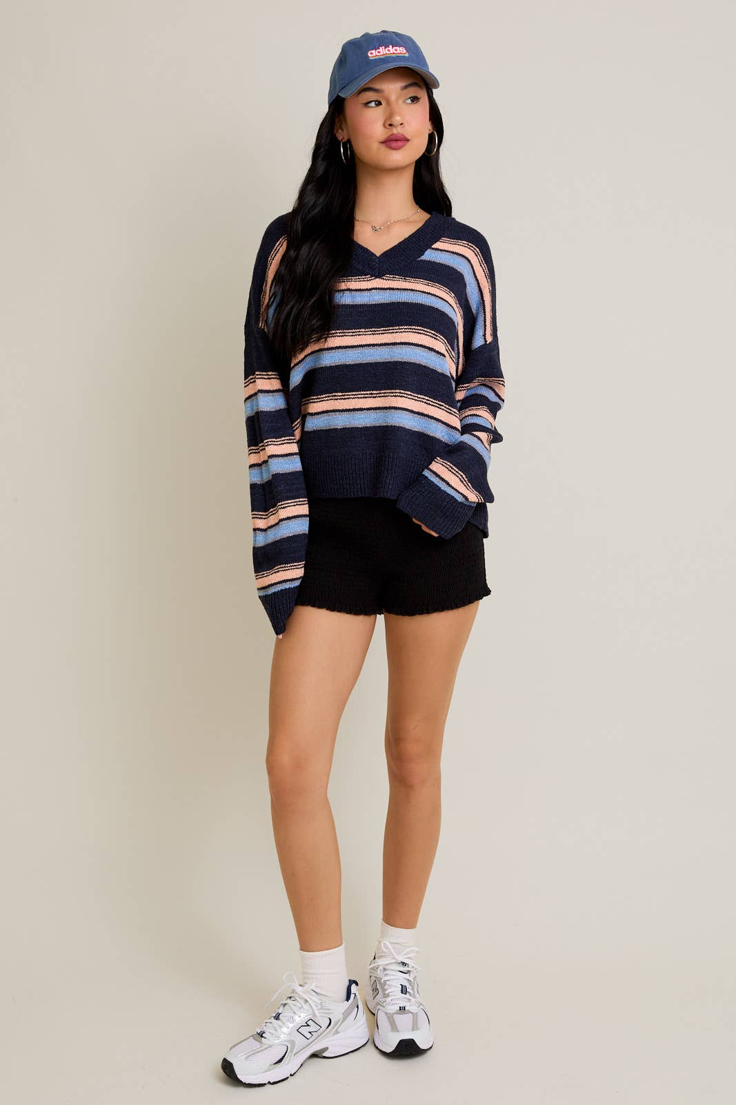 Woman wearing a striped sweater, black shorts, and white sneakers on a plain background