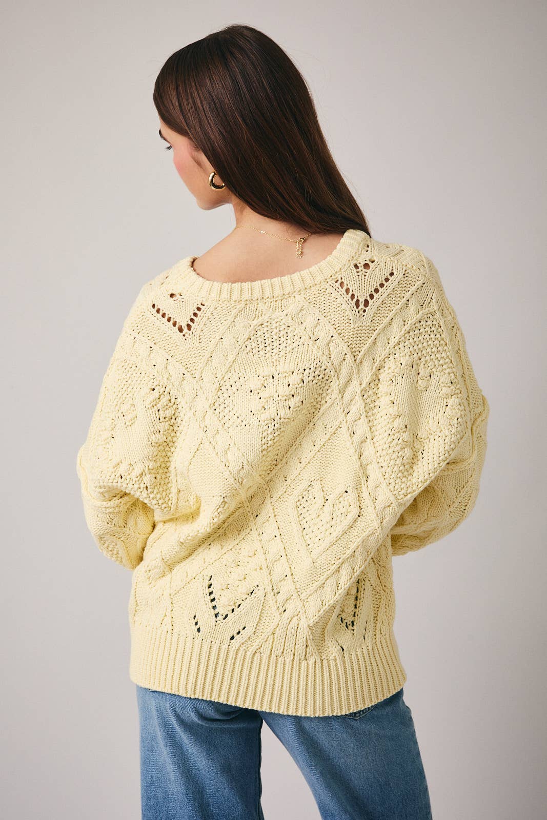 Woman wearing a light yellow knitted sweater on a plain background