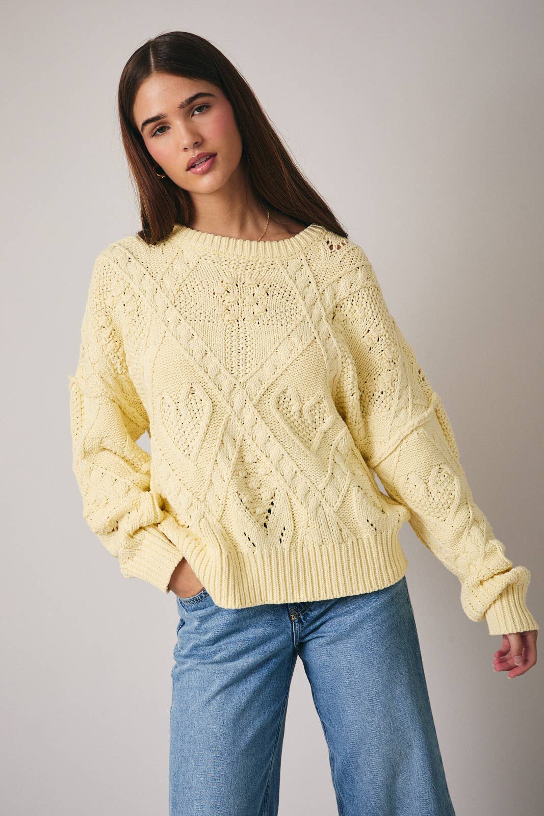 Woman wearing a light yellow knitted sweater and blue jeans against a plain background