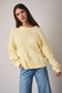 Woman wearing a light yellow knitted sweater and blue jeans against a plain background